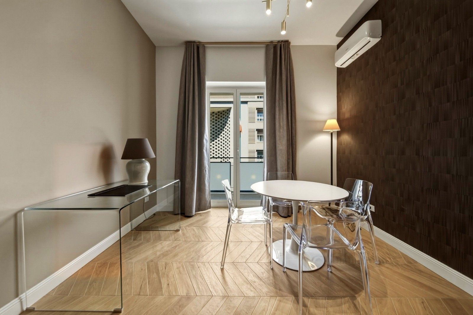 A modern kitchen with a dining area, a view through a glass door, and a wooden floor.
