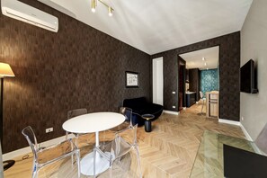 Un salon moderne avec une table ronde, des chaises transparentes, un canapé foncé et un parquet à motifs chevrons.