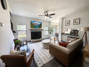 A living room with a fireplace, sofa, coffee table, and a painting above the fireplace. - Mid-Century Hideaway - Near SeaWorld (San Antonio)