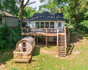 Een huis met twee verdiepingen, een terras, een overdekte buitenzitplaats en een houten vatstructuur.