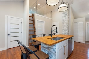 A modern kitchen with a wooden island, white cabinetry, and a stone accent wall. - Riverfront oasis. Scandinavian sauna. Great fishing. (lyndon)