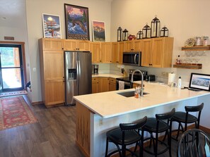 A modern kitchen with wooden cabinets, stainless steel appliances, a large island with bar stools, and decorative items on the wall. - Perfect 3-bedroom condo in Big Sky for your next getaway with relaxing hot tub (Big Sky)