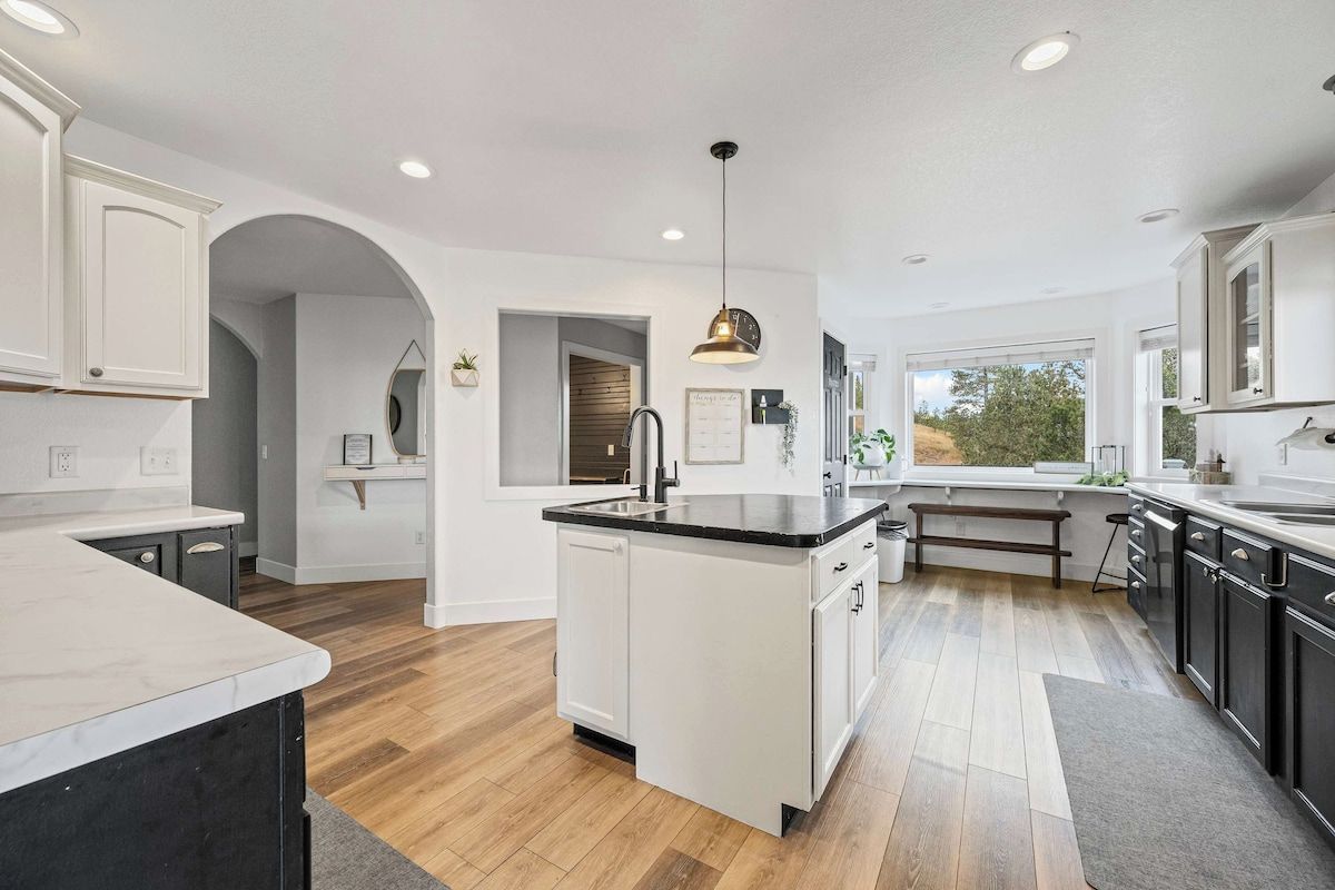 A modern kitchen with white cabinetry, a central island, and a large window providing natural light.