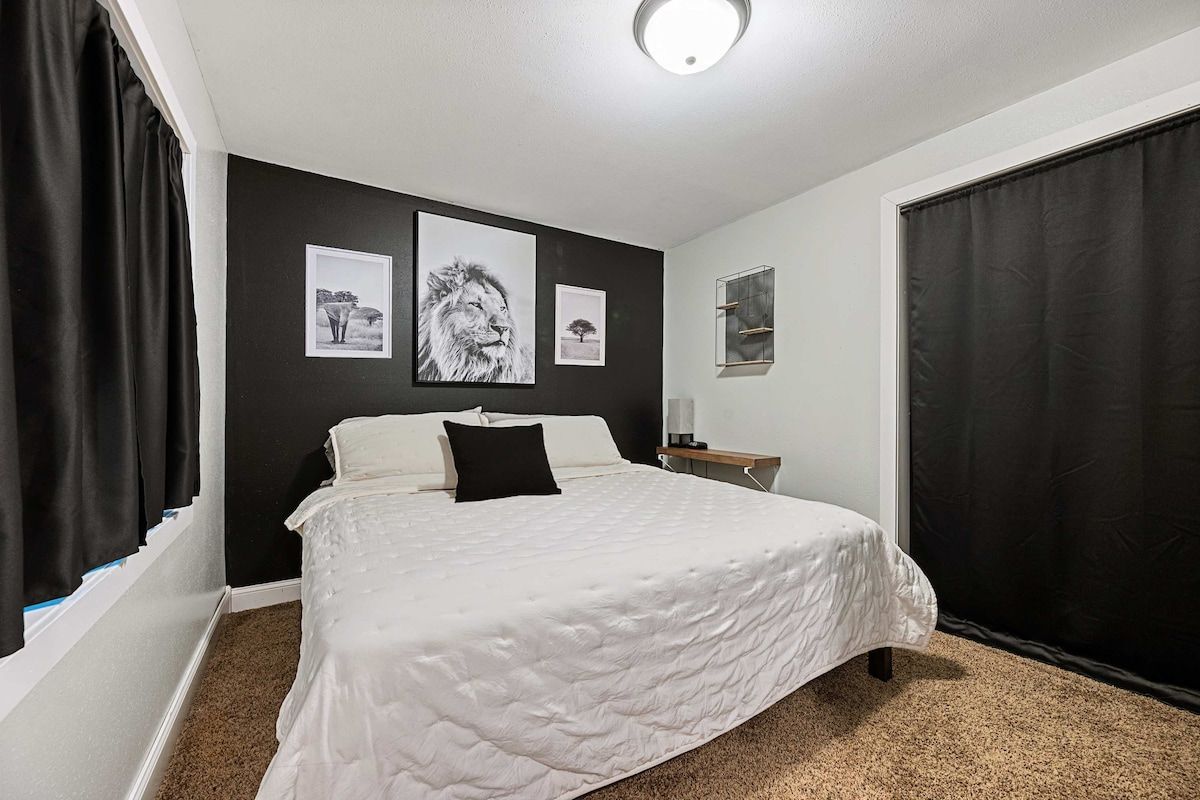 A bedroom with a large bed, a nightstand, and a window with curtains.