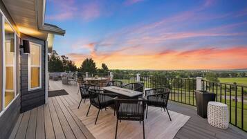 A deck with outdoor furniture, a table, and chairs, overlooking a landscape.