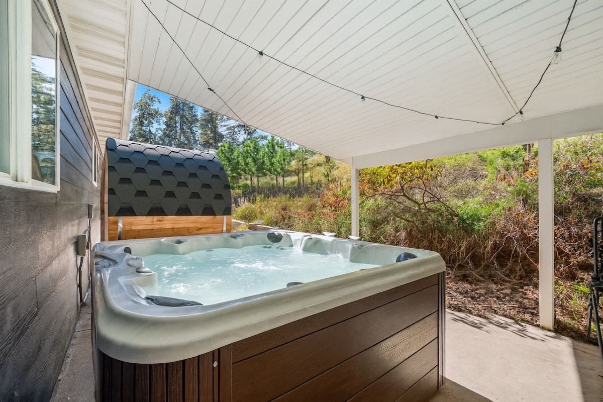 Een jacuzzi in een overdekte buitenruimte met uitzicht op bomen en struiken.
