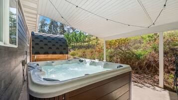 Een jacuzzi in een overdekte buitenruimte met uitzicht op bomen en struiken.