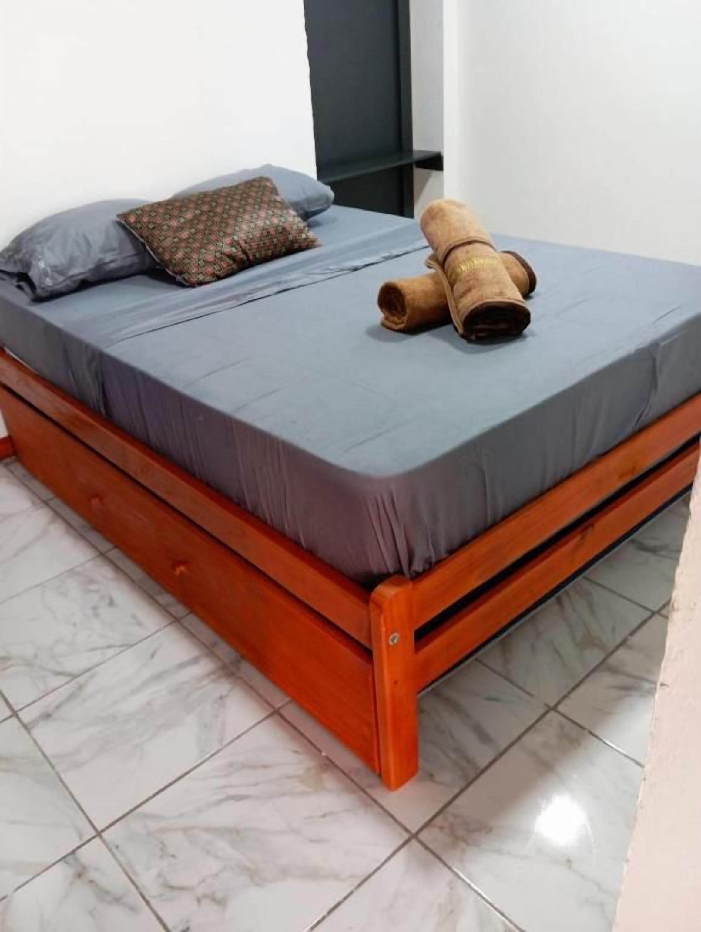 A bed with a grey mattress, a brown pillow, and a rolled-up brown blanket.