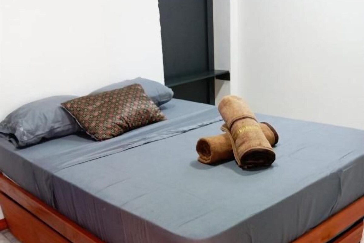A bed with a grey mattress, a brown pillow, and a rolled-up brown blanket.