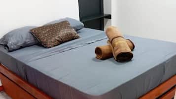 A bed with a grey mattress, a brown pillow, and a rolled-up brown blanket.