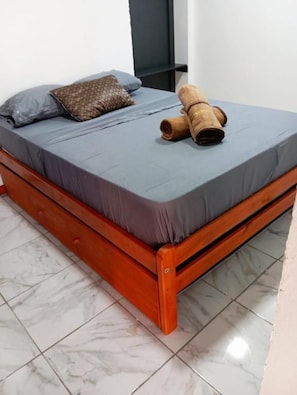 A bed with a grey mattress, a brown pillow, and a rolled-up brown blanket. - La Frontera (Puerto Iguazú)