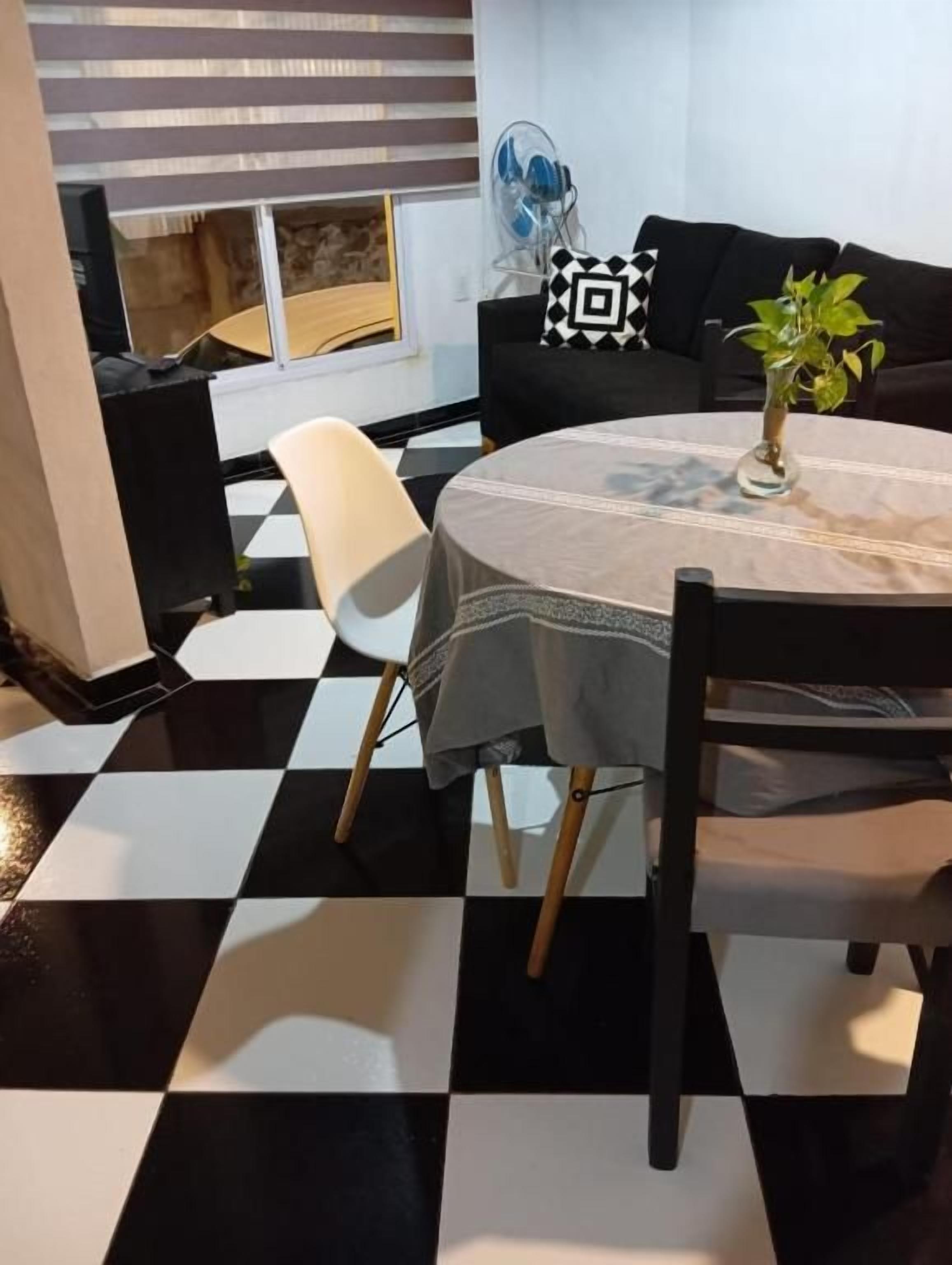 A dining area with a checkered floor, a round table with a tablecloth, and a black and white patterned sofa.