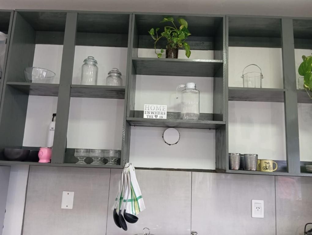 A kitchen with open shelving, glass jars, a sign stating 'HOME IS WHERE THE IS,' and hanging kitchen utensils.