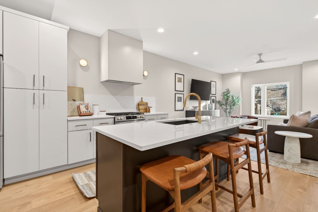 A modern kitchen with white cabinetry, a central island with bar stools, a stove, and a large window.