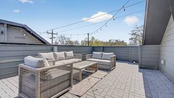 An outdoor patio with a sofa set and a wicker chair, a brick floor, and overhead string lights.