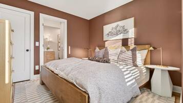 A bedroom with a bed, bedside tables, a nightstand, a wall-mounted lamp, and a door.