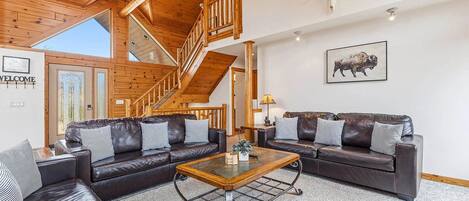 A spacious living room with a wooden staircase, leather sofas, and a mounted buffalo picture.