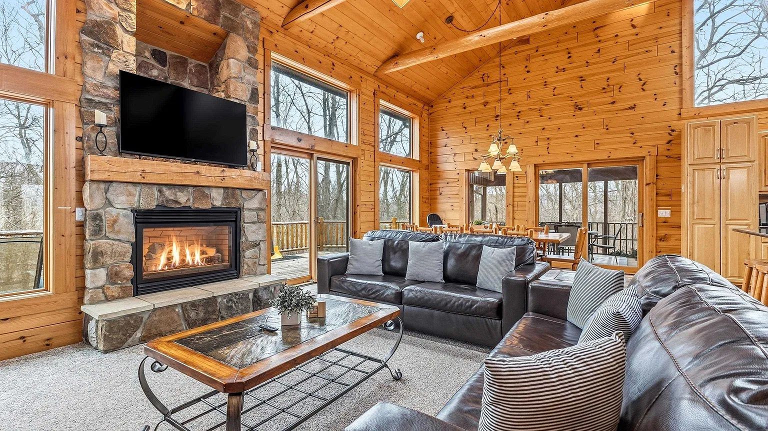 A log cabin interior with a stone fireplace, leather sofas, and a television mounted on the wall.