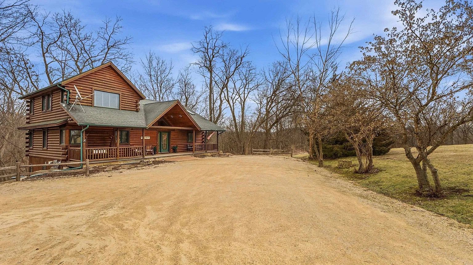 A two-story log cabin with a porch and a dirt driveway.