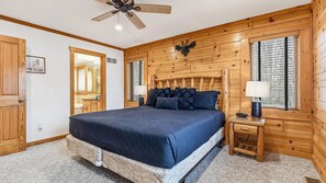 Ein Schlafzimmer mit einem großen Bett, Holzwänden, einem Deckenventilator und einem Nachttisch mit einer Lampe.