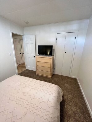 Ein Schlafzimmer mit einem Bett, einer Kommode, einem Fernseher darauf und einem Kleiderschrank.