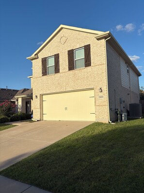 A two-story residential building with a garage, brick facade, and a clear sky. - The Wayne House - Spacious 4BR Retreat Near PGA Frisco & Universal (Aubrey)
