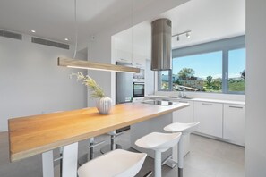 A modern kitchen with a wooden countertop, white bar stools, and a view of the outdoors. - Le Mont Blanc | 3-Bedroom Apartment with Shared Pool (Kounoupidiana)