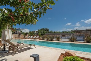 Una piscina con sillones de descanso y un muro de piedra al fondo.