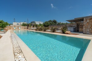 Ein rechteckiger Swimmingpool mit klarem, blauem Wasser, umgeben von einer Steinmauer und einer gepflasterten Liegefläche.