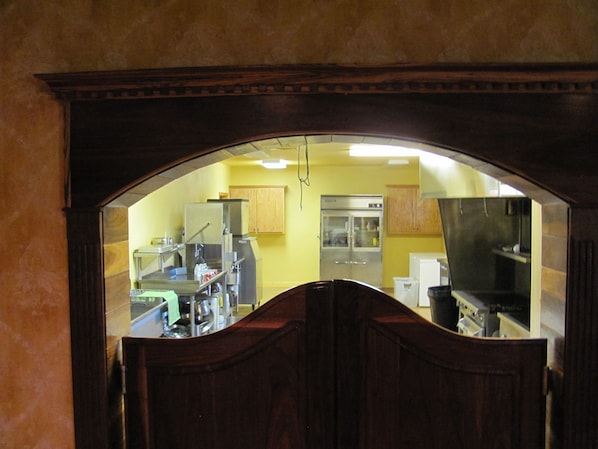 A view through a wooden archway into a kitchen with yellow walls, stainless steel appliances, and wooden cabinets.