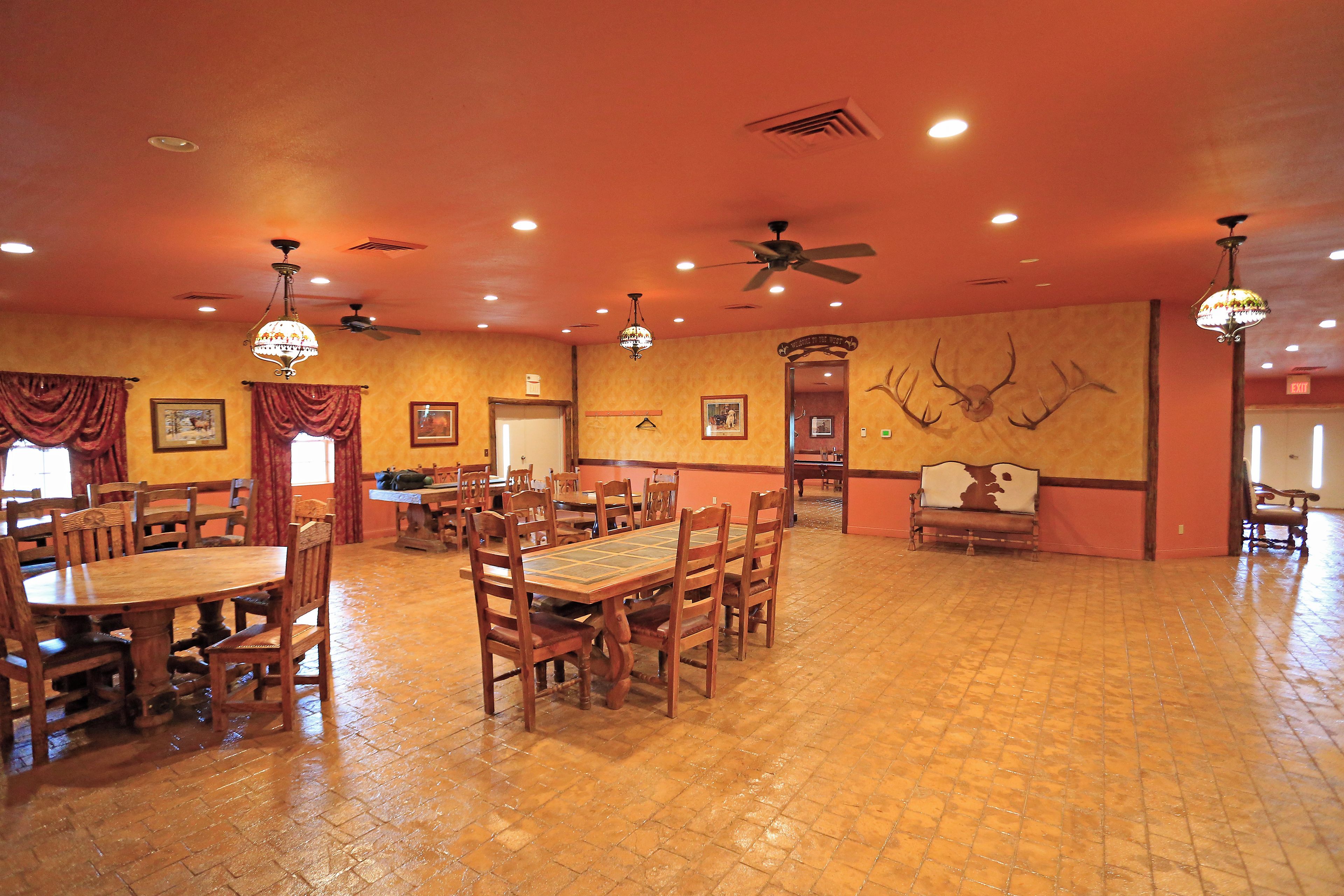 A spacious dining area with wooden tables and chairs, ceiling fans, and a wall-mounted deer head decoration.