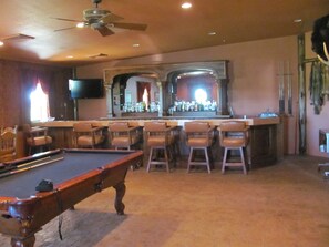 A bar area with a pool table, bar stools, and a television mounted on the wall.