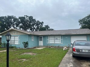 A single-story house with a garage, a front yard with grass, and a parked car. - Spacious 4-bedroom house in the enchanting Silver Springs Shores (Ocala)