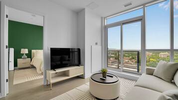 A modern living room with a large TV, a sofa, a round coffee table, and a view of a cityscape through large windows.