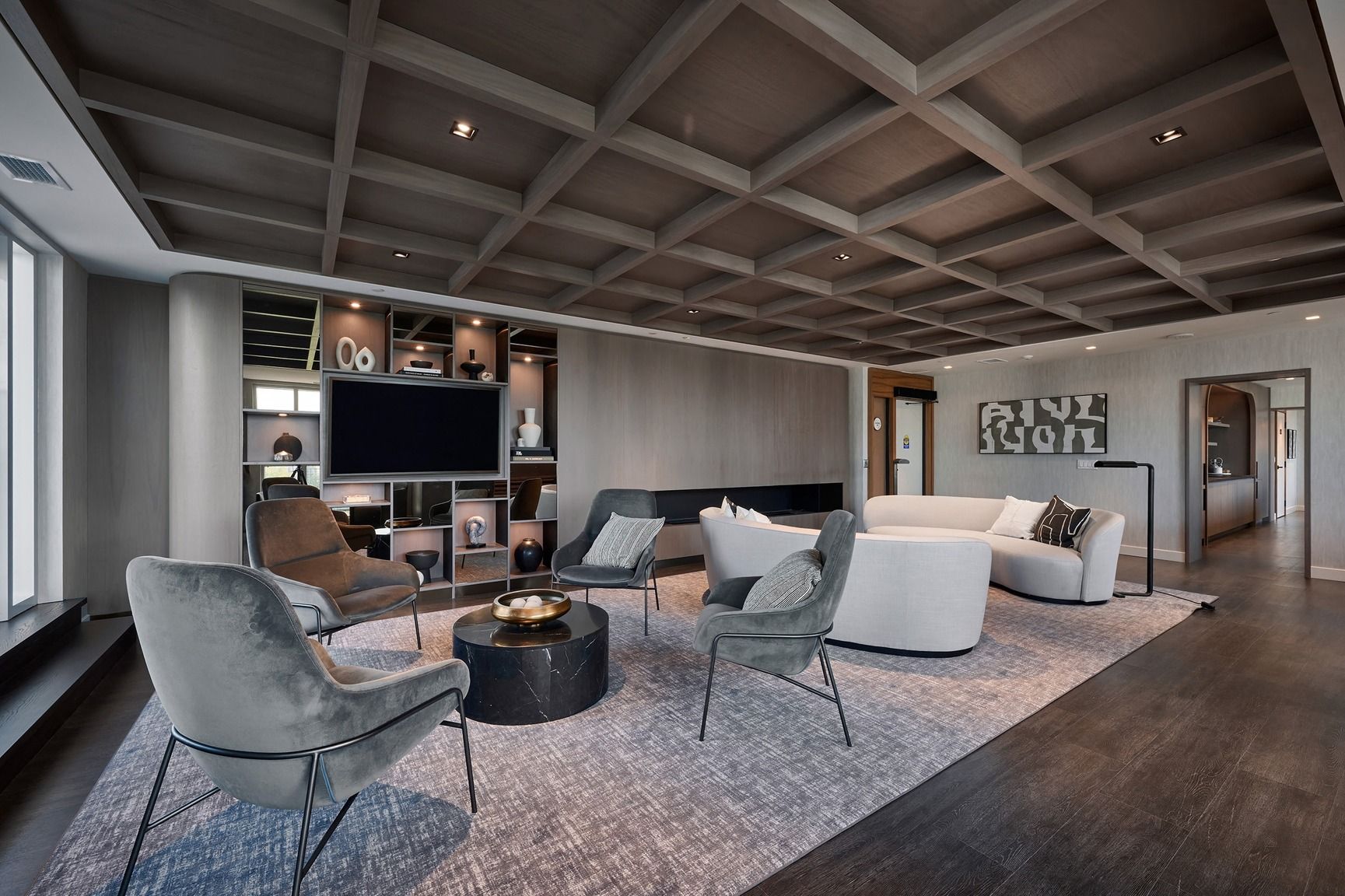 A modern living room with a high ceiling, built-in shelving, a flat-screen TV, and a seating area with a coffee table.