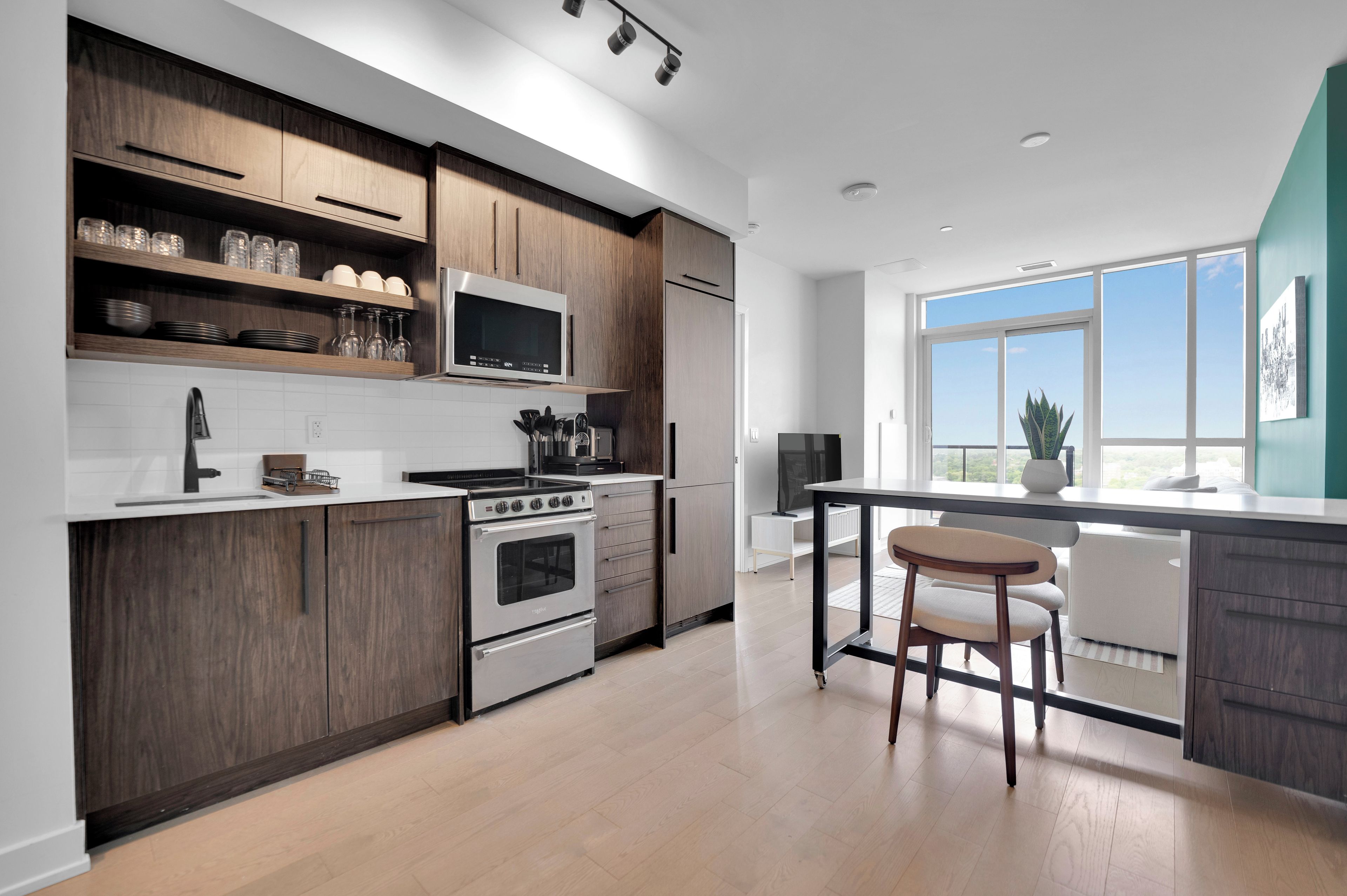 A modern kitchen with wooden cabinets, a stainless steel stove, and a large window providing a view of the outdoors.