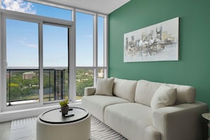 Ein modernes Wohnzimmer mit großem Fenster, grüner Wand und Blick auf die Stadt.