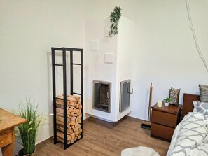 A bedroom with a fireplace, a bed with patterned bedding, a nightstand with a candle, and a wooden shelf with logs. - Bergzeit-Stoder by Interhome (Hinterstoder)