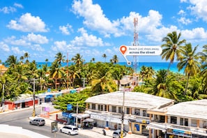 A coastal street with buildings, palm trees, and a clear blue sky. - Apartment with a Pool Just Steps from the Beach and Restaurants, Central Location (Punta Cana)
