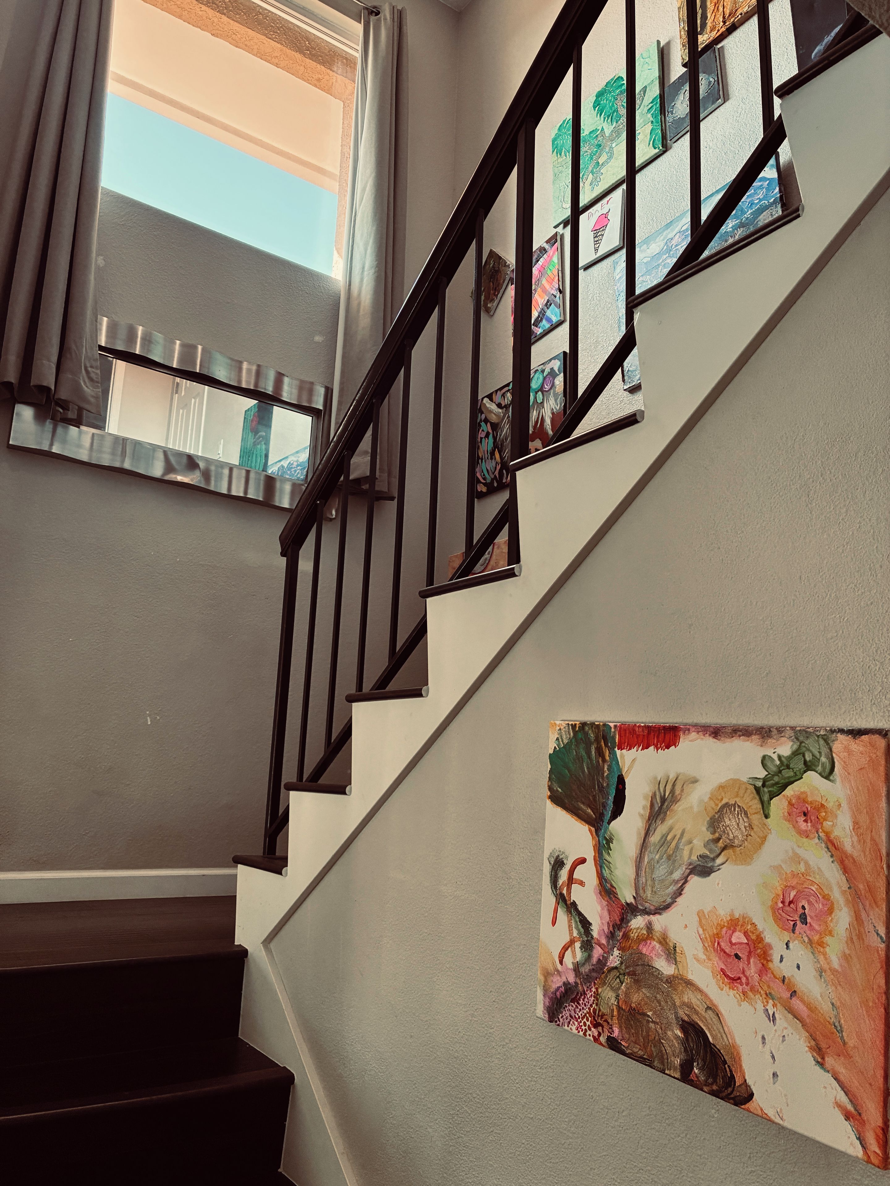 A staircase with a handrail, a painting on the wall, and a window with curtains.