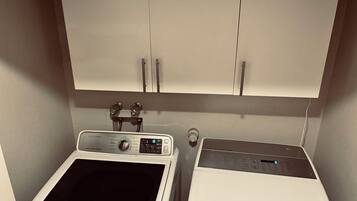 A laundry area with a washing machine and dryer, a cabinet above, and a control panel on the washing machine.