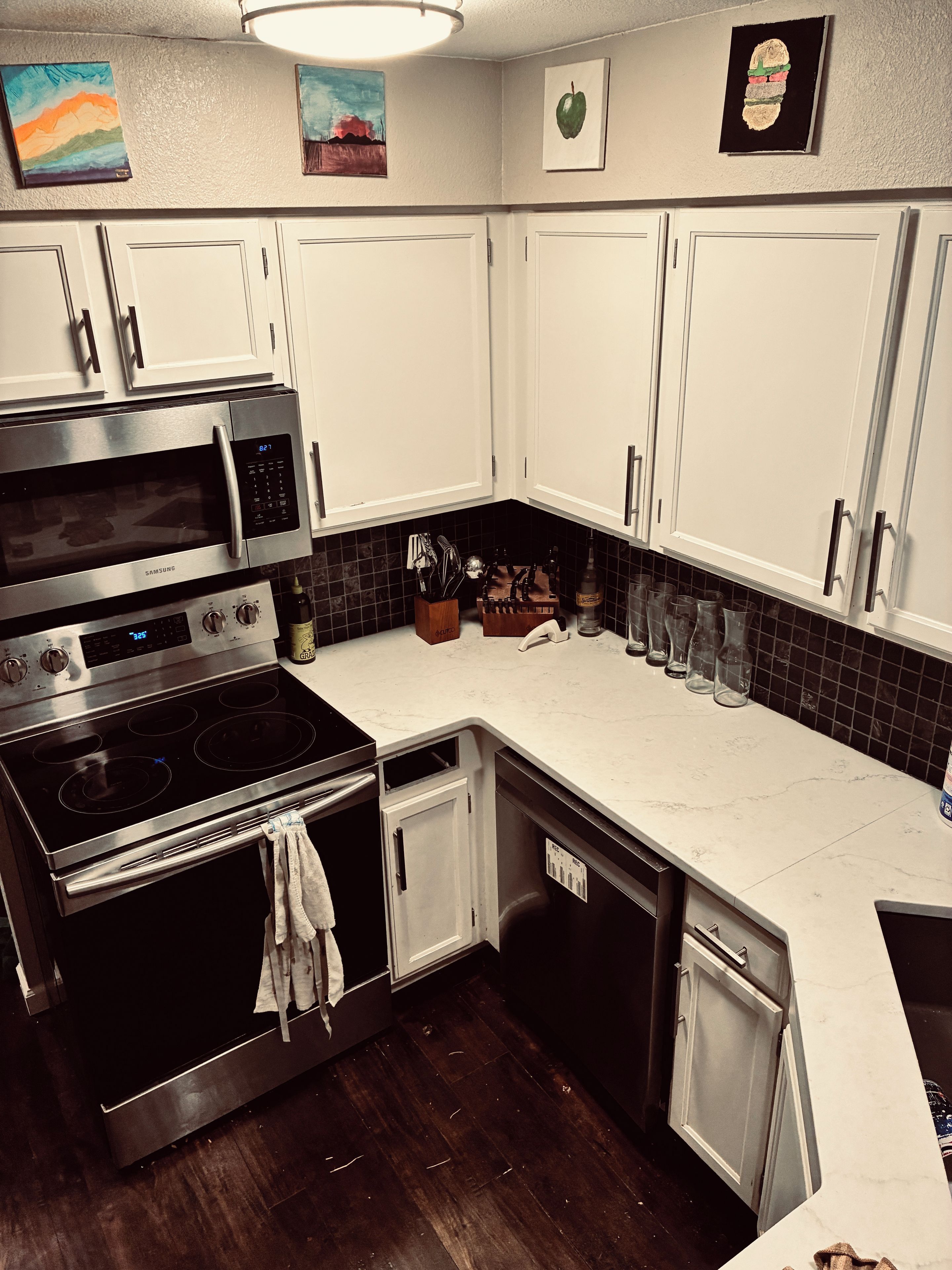 A modern kitchen with stainless steel appliances, white cabinets, and a black tiled backsplash.