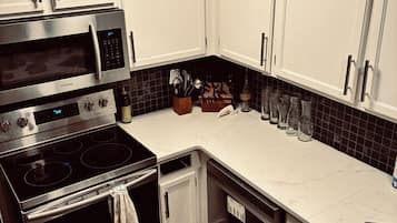 A modern kitchen with stainless steel appliances, white cabinets, and a black tiled backsplash.