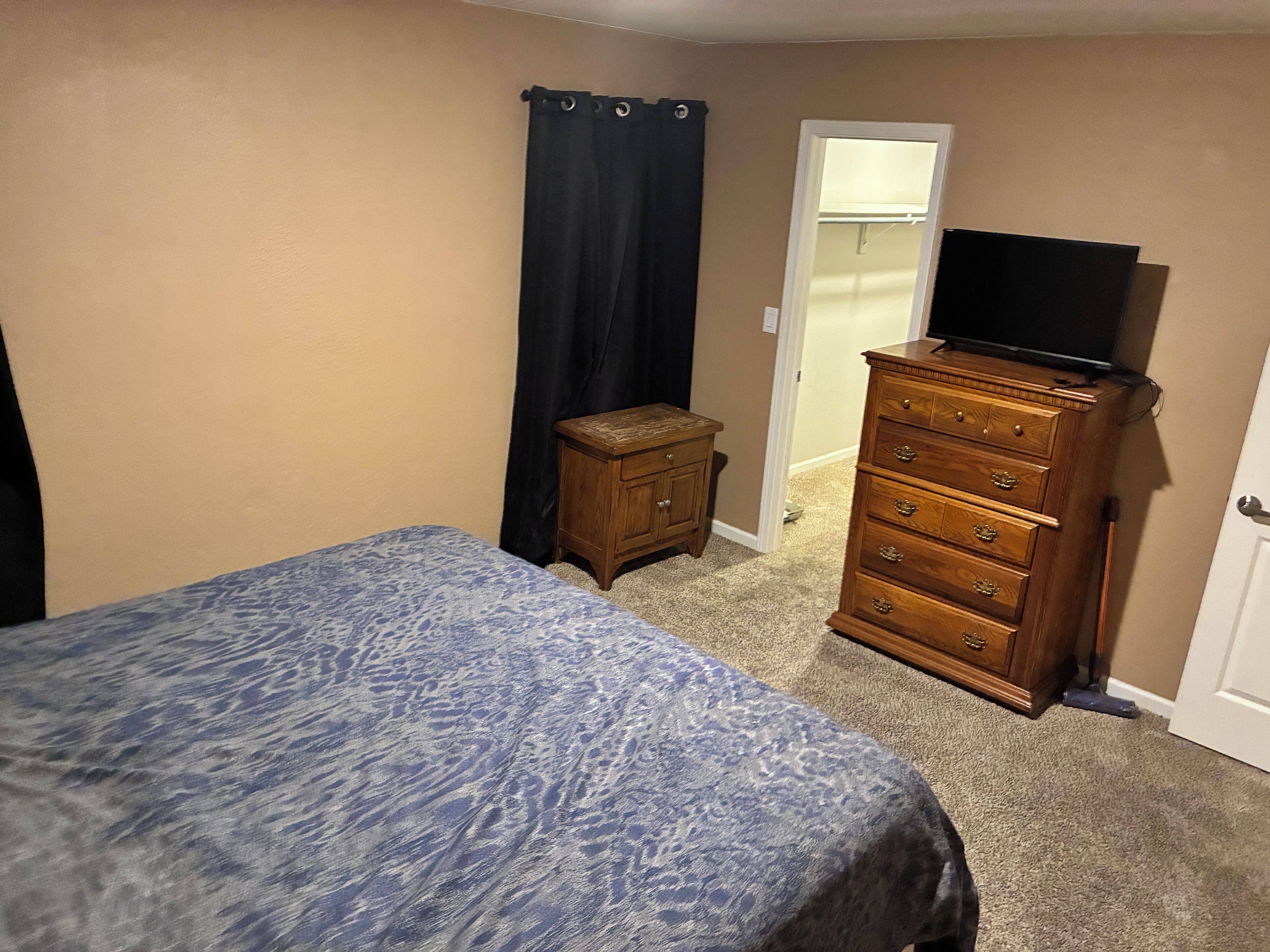 A bedroom with a bed, a dresser, a television on top, and a closet.
