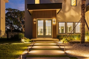A modern house with a front entrance, a staircase, and a well-lit pathway leading to the door.