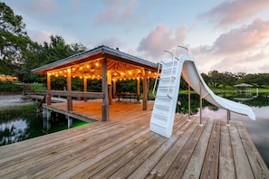 Een houten terras met een glijbaan, een overdekte zithoek en een vijver.