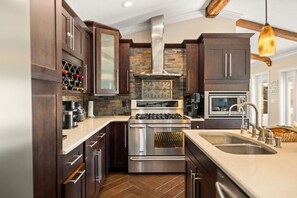 A modern kitchen with dark wood cabinets, stainless steel appliances, a stone backsplash, and a herringbone-patterned floor.