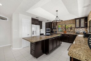 A modern kitchen with dark cabinetry, granite countertops, and a central island. - Lakefront Estate 16ppl |Pool| Sauna| Dock| Hot Tub (Sebring)