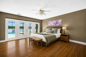 A bedroom with a bed, bedside tables, a bench, a ceiling fan, and a view of a swimming pool through glass doors. - Lakefront Estate 16ppl |Pool| Sauna| Dock| Hot Tub (Sebring)