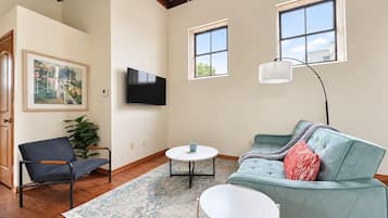 A living room with a sofa, a chair, a coffee table, and a TV mounted on the wall.